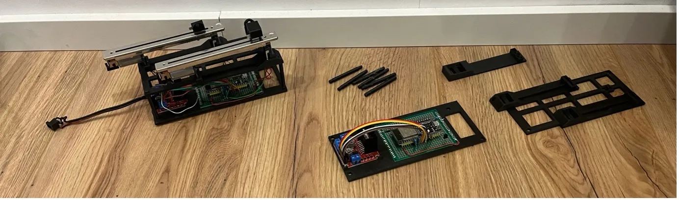 The electronics of an early prototype laid out on the floor: motorfader assembly, ESP32 on a breadboard shield, and 3D-printed mounting parts.