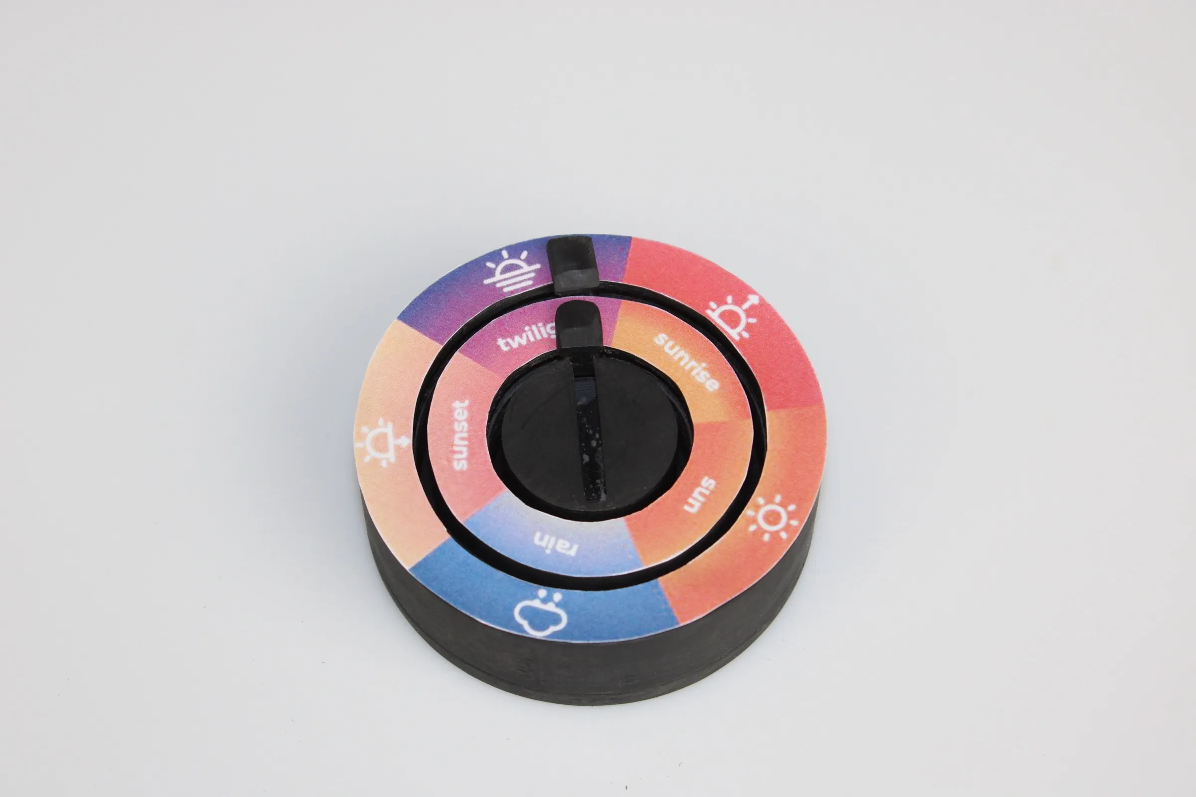 The hub in ambience mode: a printed ring divided into five labelled segments, sunrise, sun, rain, sunset and twilight, each with a weather icon, around a black central slider.