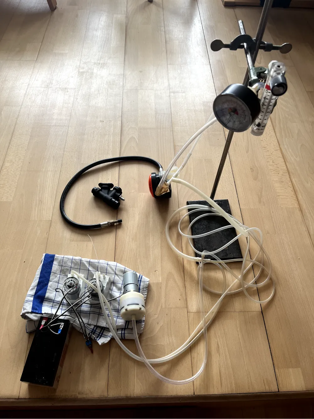A bench test on a wooden floor: a pressure gauge clamped to a stand, clear tubing looped to a filter cartridge, a regulator and mouthpiece laid out alongside.