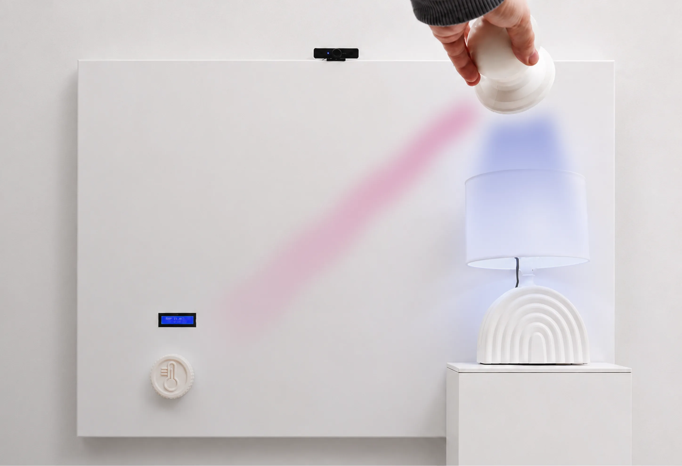 A hand lifting the doorknob-shaped controller in front of a white wall panel with a thermostat dial, next to a glowing lamp.