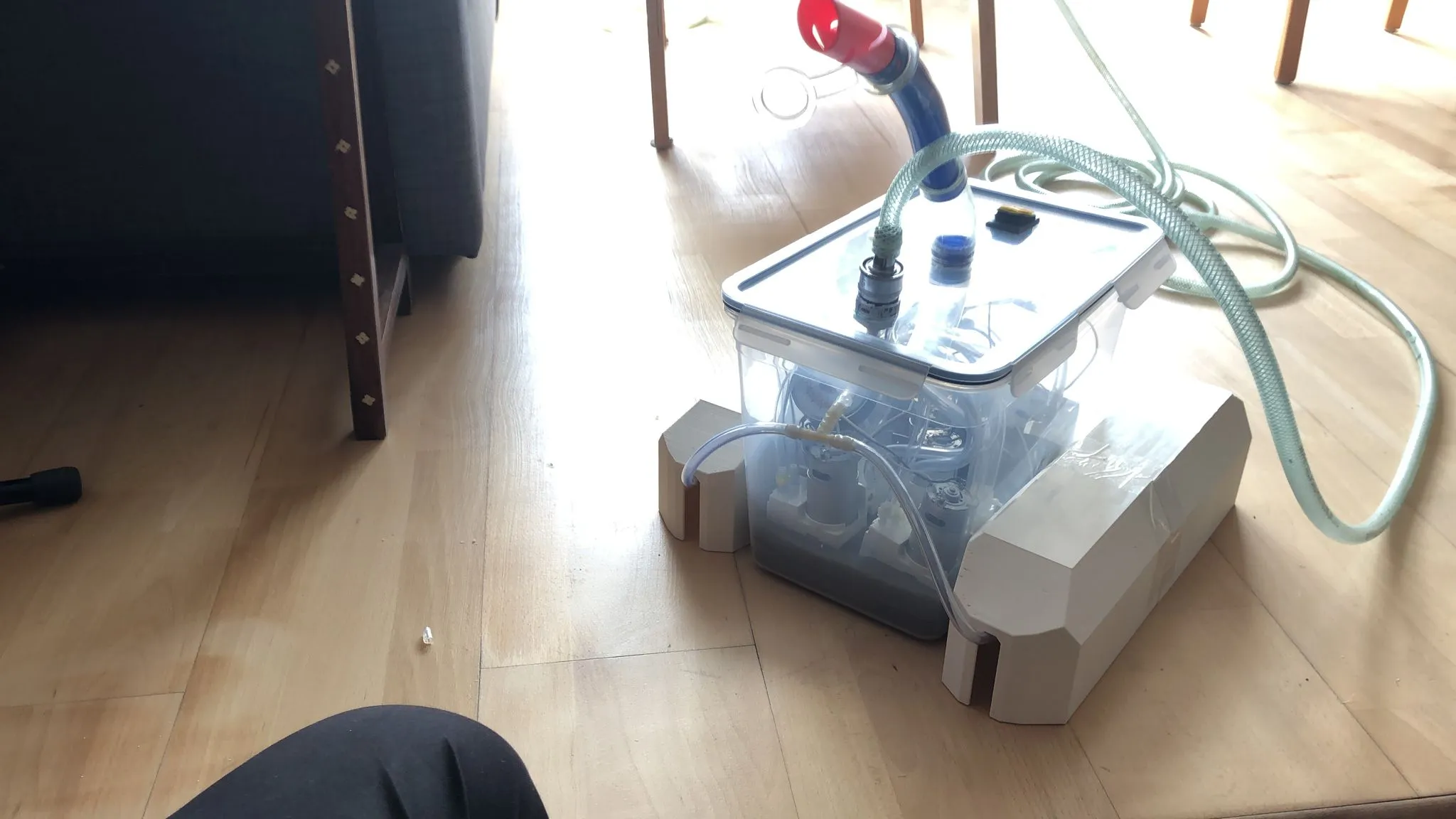 The floating reservoir: a clear plastic box holding bottles, braced between white foam floats, with a red-topped corrugated intake hose running out of it.
