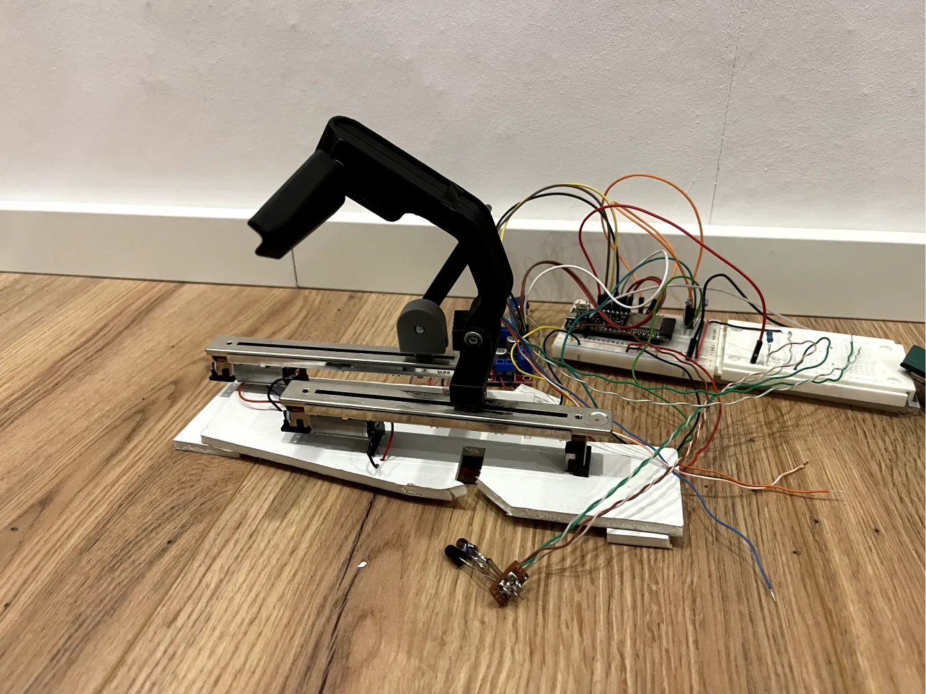 The physical prototype on a wooden floor: a black handle mounted to a motorised fader rail, with a pivot, ribbon wiring and a microcontroller board alongside.