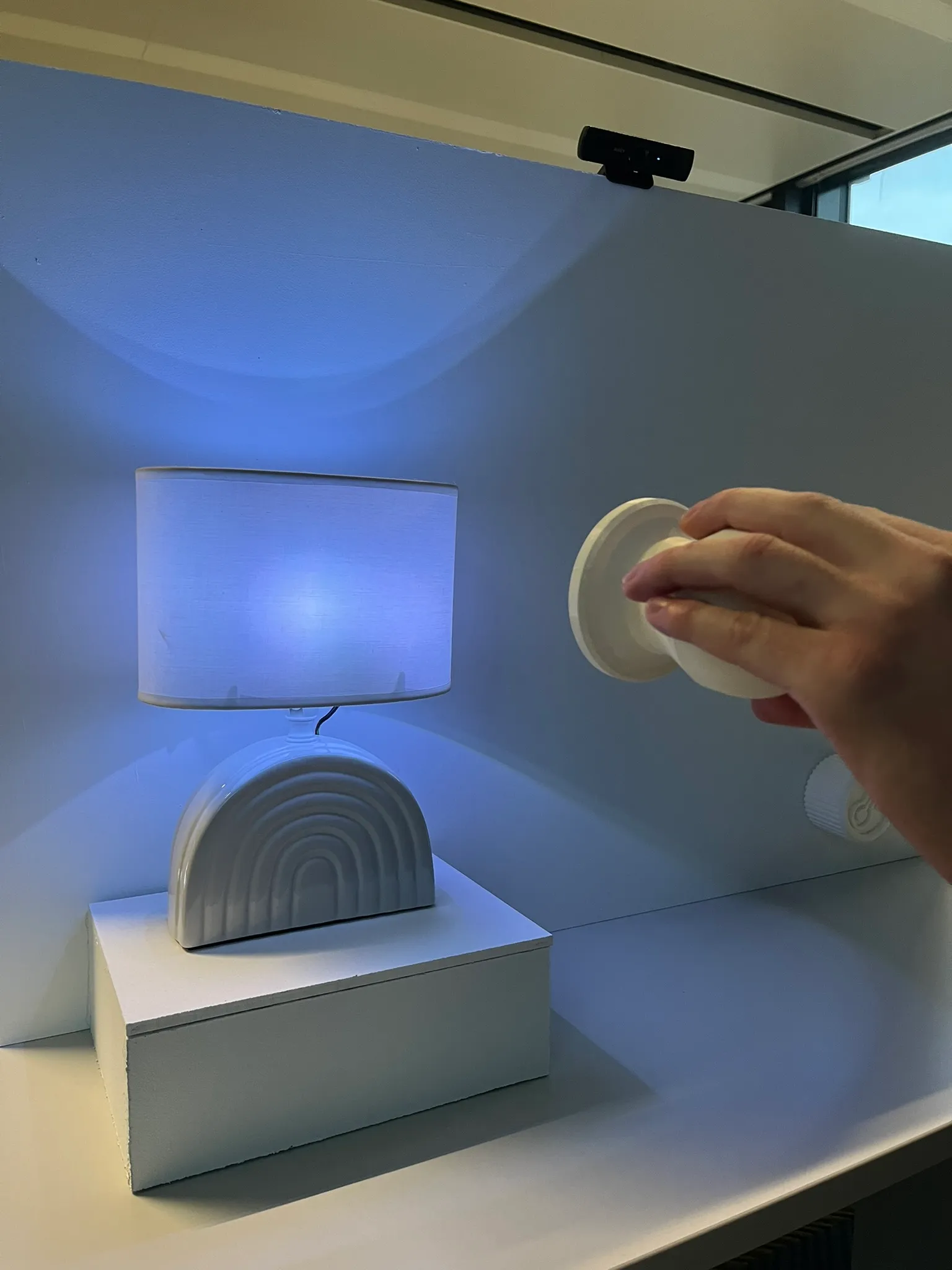 Close view of a hand tilting the white controller toward the glowing lamp, the camera mounted above in frame.