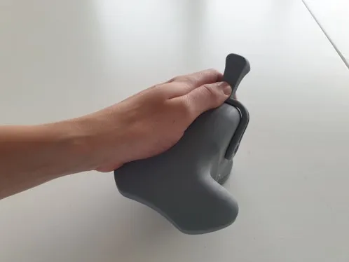 The finished grey prototype held in a hand: the palm resting on the wide upper surface, fingers curled under the throttle lever.
