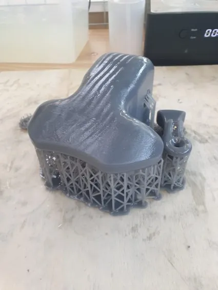 The grey resin-printed control unit fresh off the printer, still sitting on its lattice of support structures, on a workbench beside a wash station.