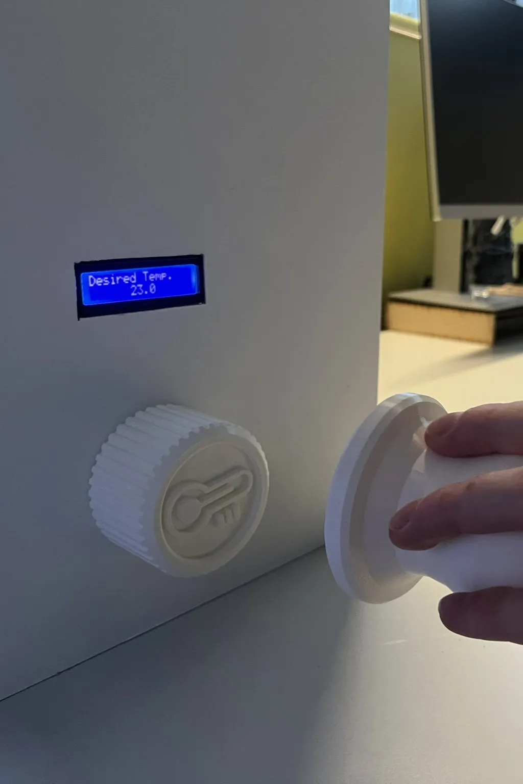 The thermostat side of the wall: a blue LCD reading Desired Temp 22.0 above a white knurled dial with a thermometer icon, the controller held alongside.