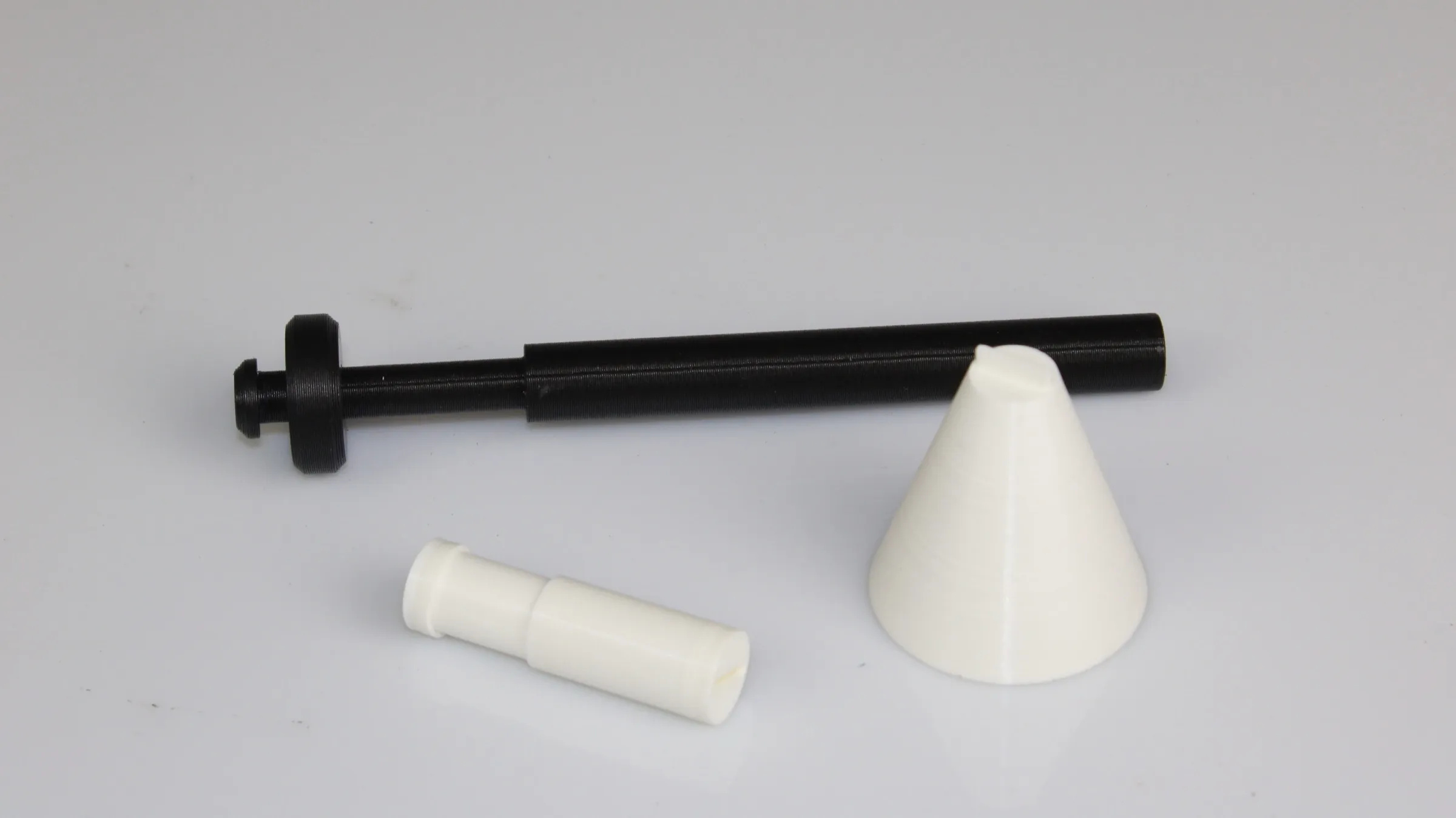 The 3D-printed wand in parts: a black shaft with a sliding collar, a separate white sleeve, and a white conical lamp shade form.
